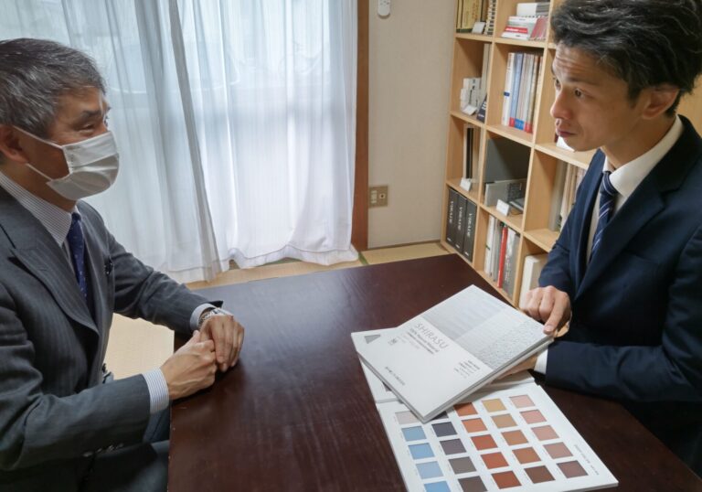 色見本帳を机に広げ、シラス壁の話に花を咲かせる高千穂シラス佐藤様とリアルカラー社長